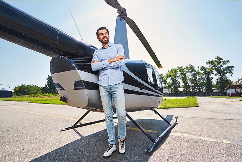 Full-length portrait of smiling confident young male leaned against private helicopter looking away